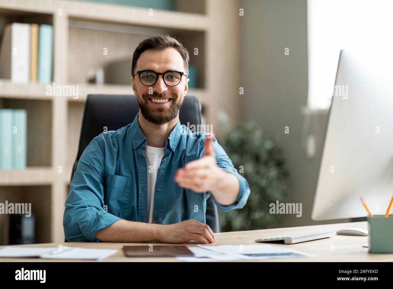 Handsome Businessman Giving Hand For Handshake At Camera While Sitting At Desk Stock Photo