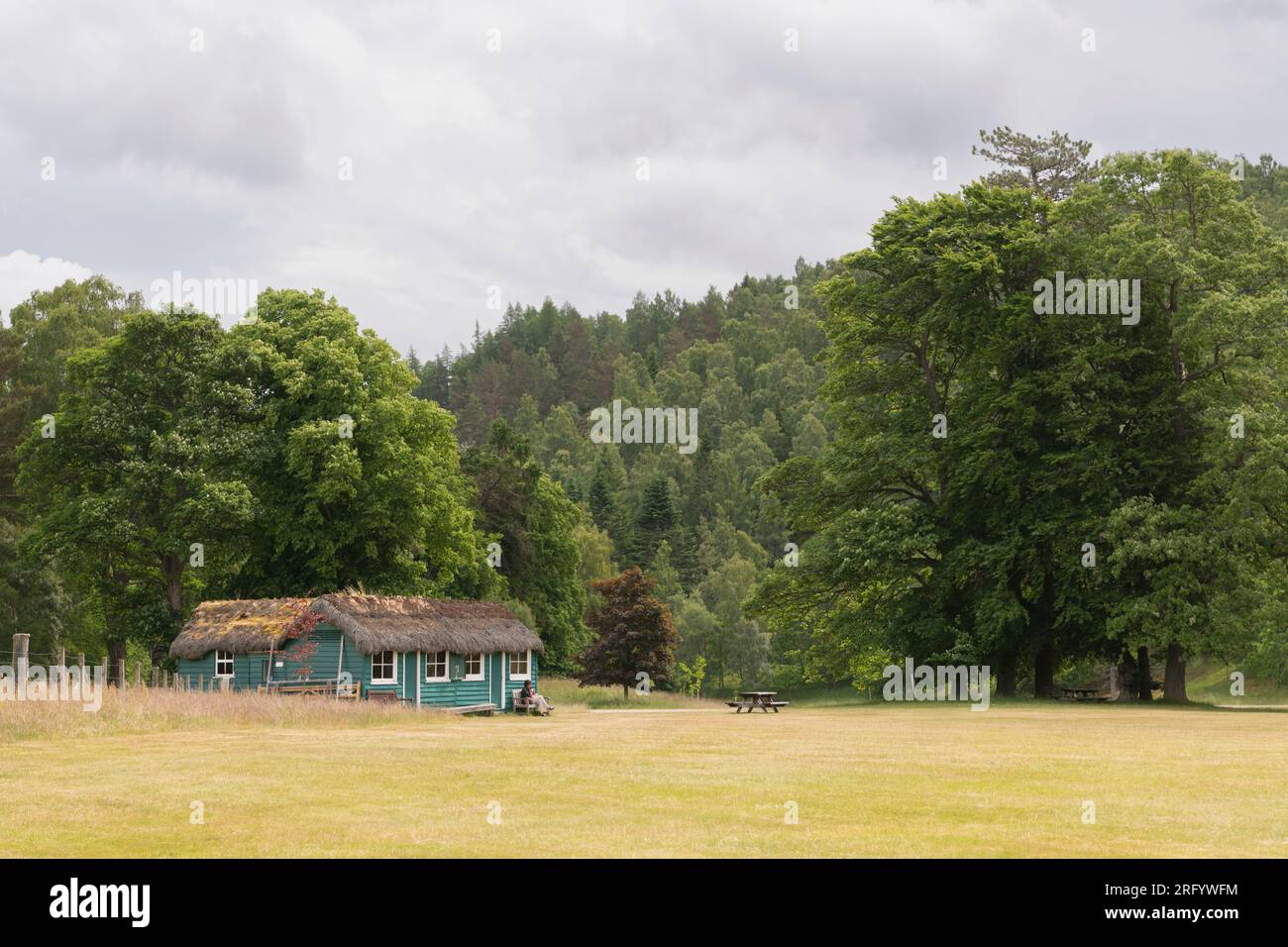 A Visitor Sitting on a Bench Outside the Thatched Cricket Pavillion in the Grounds of Balmoral Castle on Royal Deeside Stock Photo