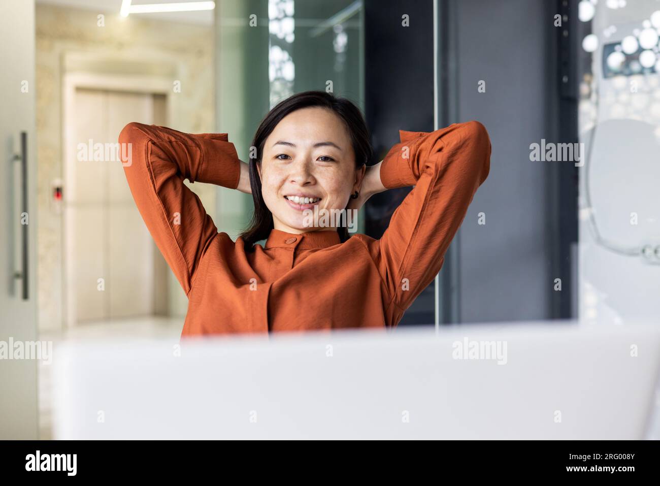 Young Asian woman resting in the office, successfully completed the work, satisfied with the results of the achievement, put her hands behind her head, dreaming, looking at the laptop screen. Stock Photo