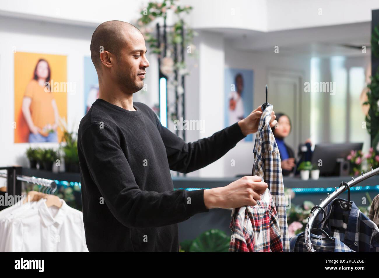 Arab man standing in mall clothing store, searching for plaid shirt and ...