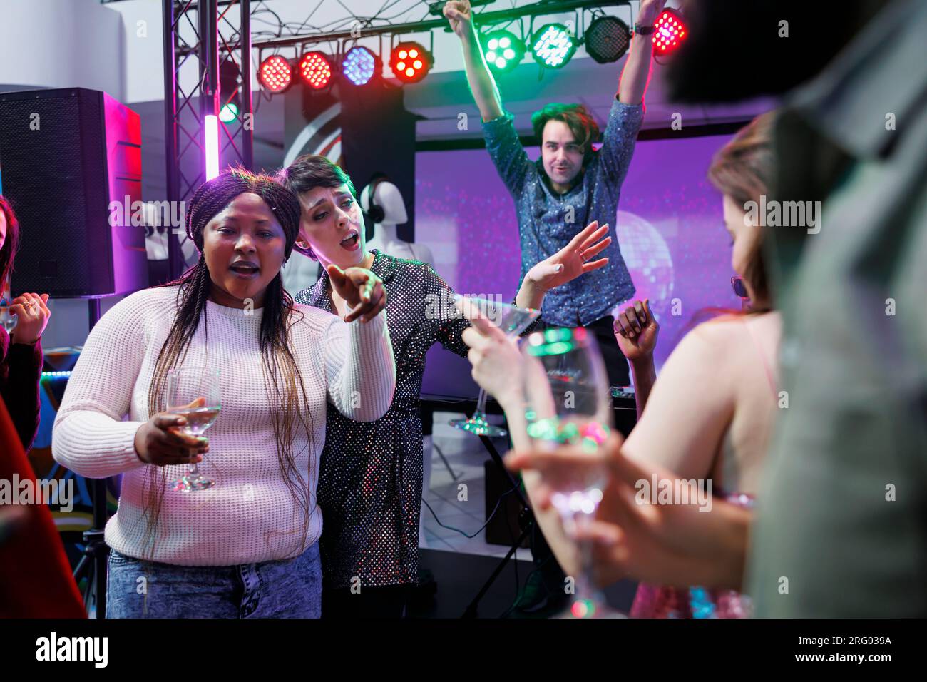 People drinking alcohol, dancing and singing at nightclub party with live music. Cheerful crowd relaxing, enjoying beverages and having fun on dancefloor at social gathering in club Stock Photo
