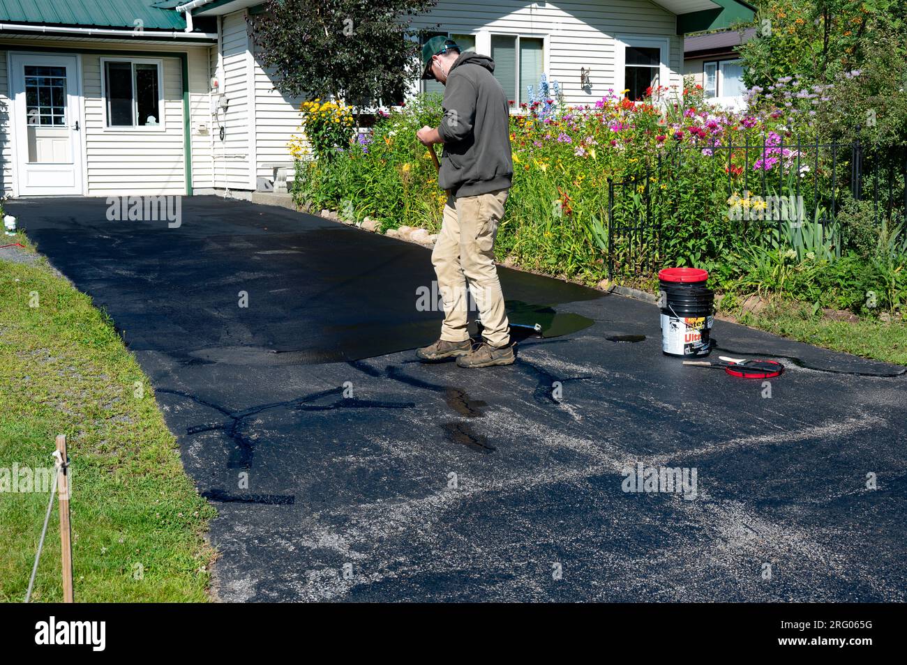 Worker spreading driveway sealer to seal cracks in an asphalt driveway