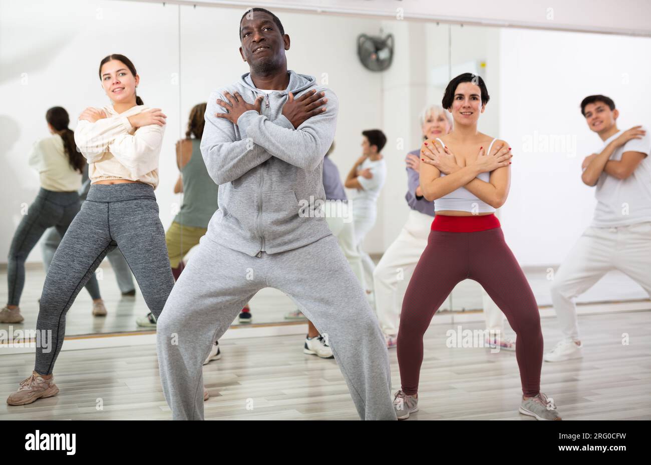 Smiling adults of different nationalities train movements in jazz dance