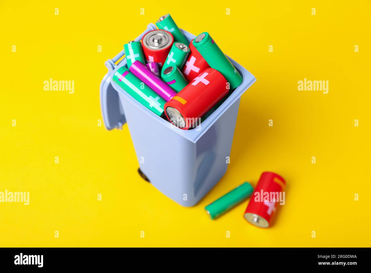 Many used batteries in recycling bin on yellow background Stock Photo