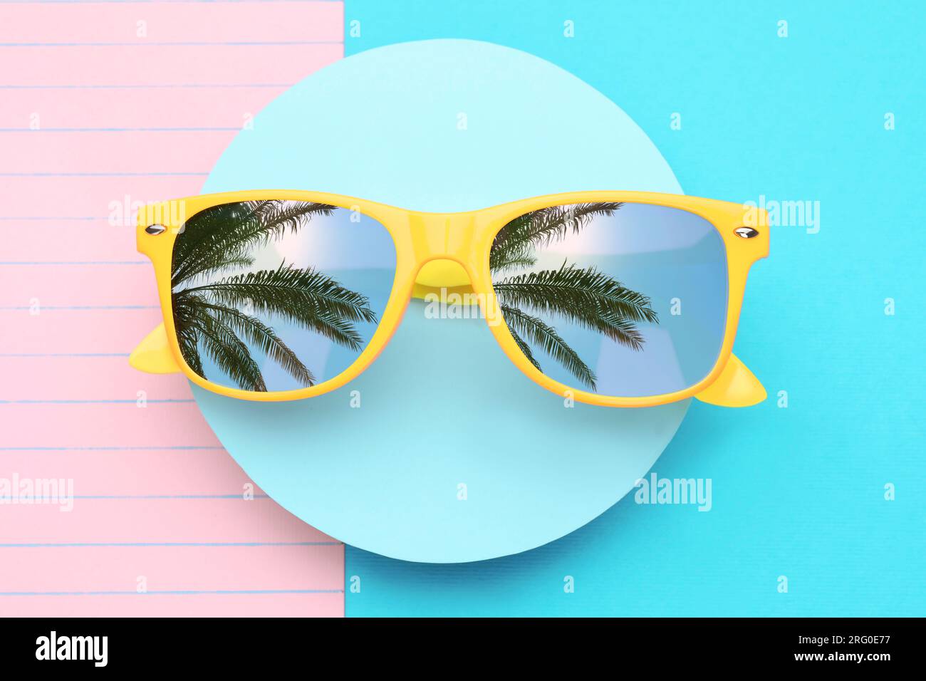 Stylish sunglasses on color background, top view. Sky and palm tree leaves reflecting in lenses Stock Photo