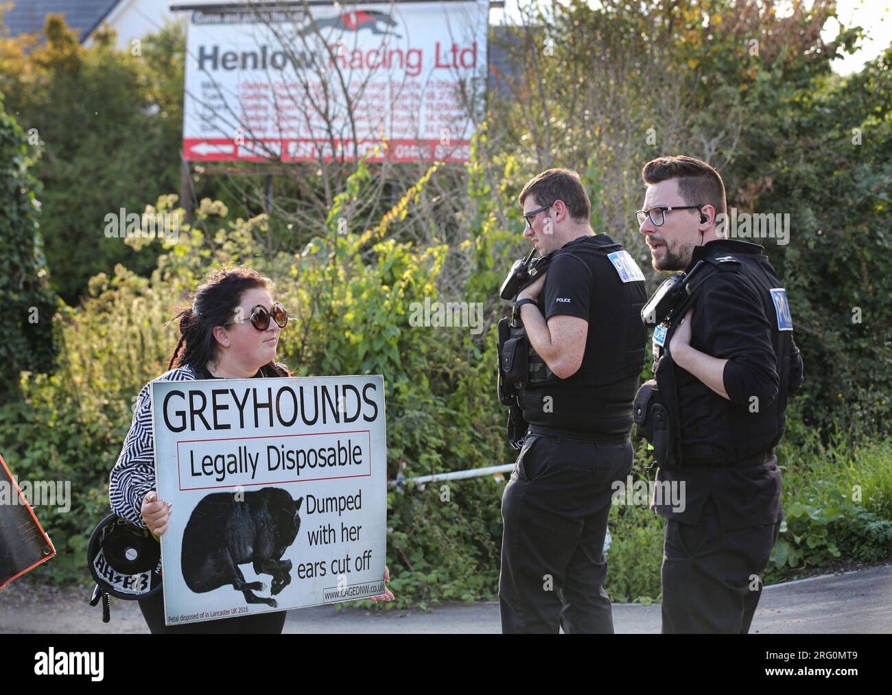 Henlow, UK. 06th Aug, 2023. A protester holding a placard reading 'Greyhounds Legally Disposable' outside the dog stadium is approached by police officers during the demonstration. Animal Rights activists protest outside Henlow dog racing track. They are aiming to highlight the cruelty associated with dog racing. In 2021 there were 4422 injuries and 120 deaths on registered greyhound race tracks in the UK. Credit: SOPA Images Limited/Alamy Live News Stock Photo