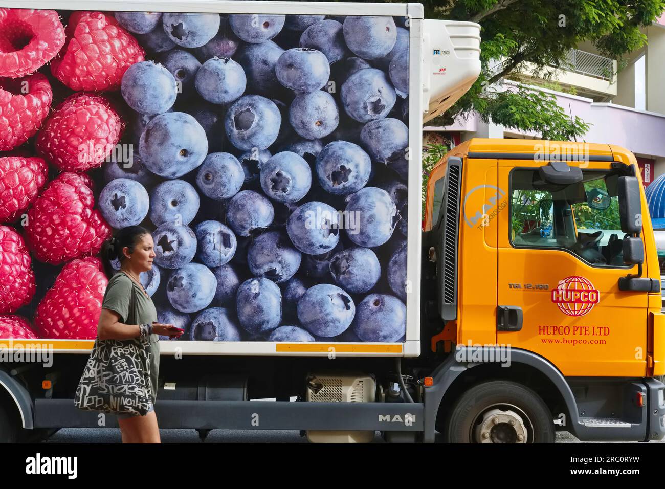 A woman passes a delivery truck of a company selling fruit and berry jams, with a large photo of blueberries and raspberries on its side; Singapore Stock Photo