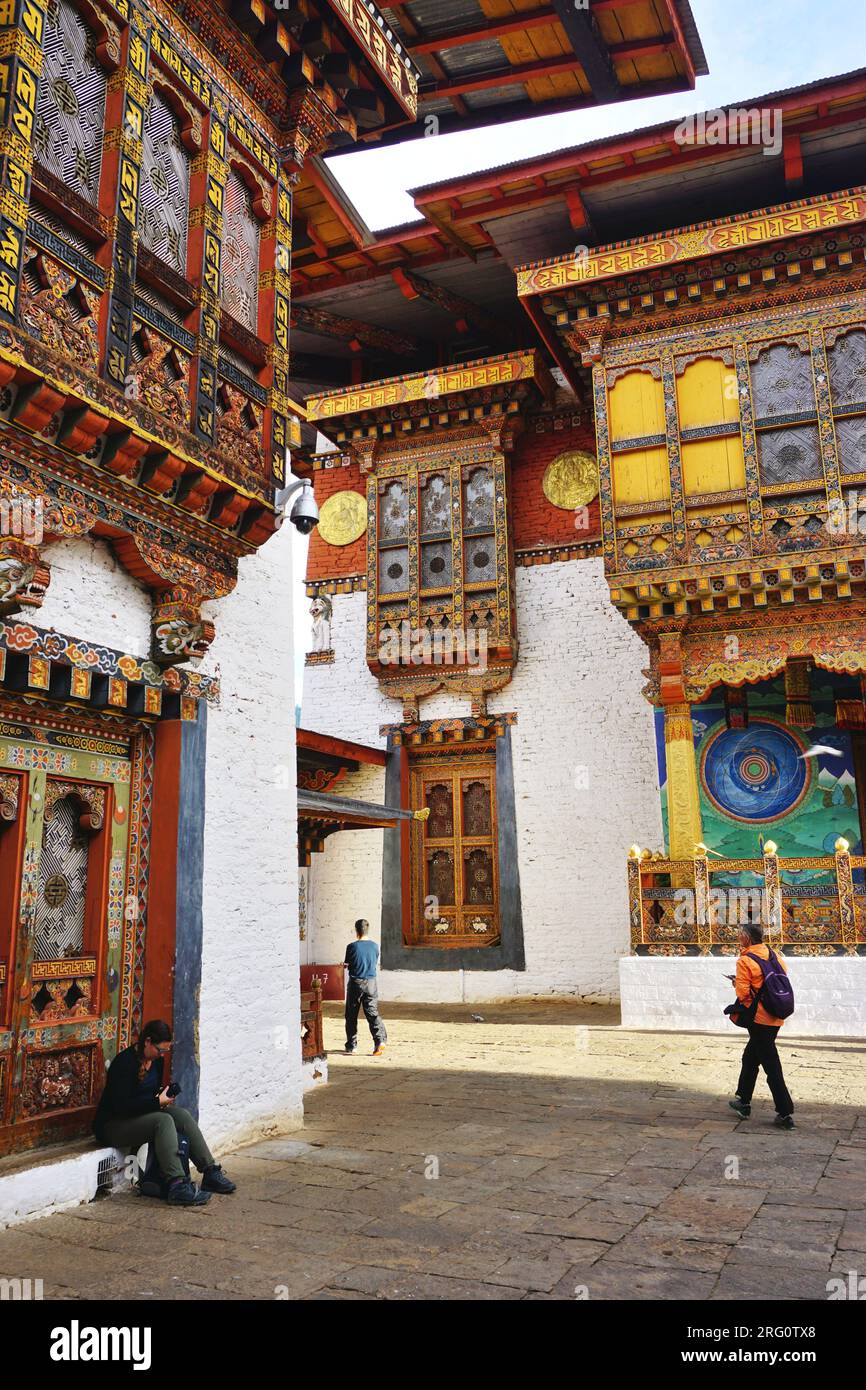 Visitors walk past ornate carved and painted historic wooden and stone buildings on the grounds of Punakha Dzong, in the Kingdom of Bhutan Stock Photo