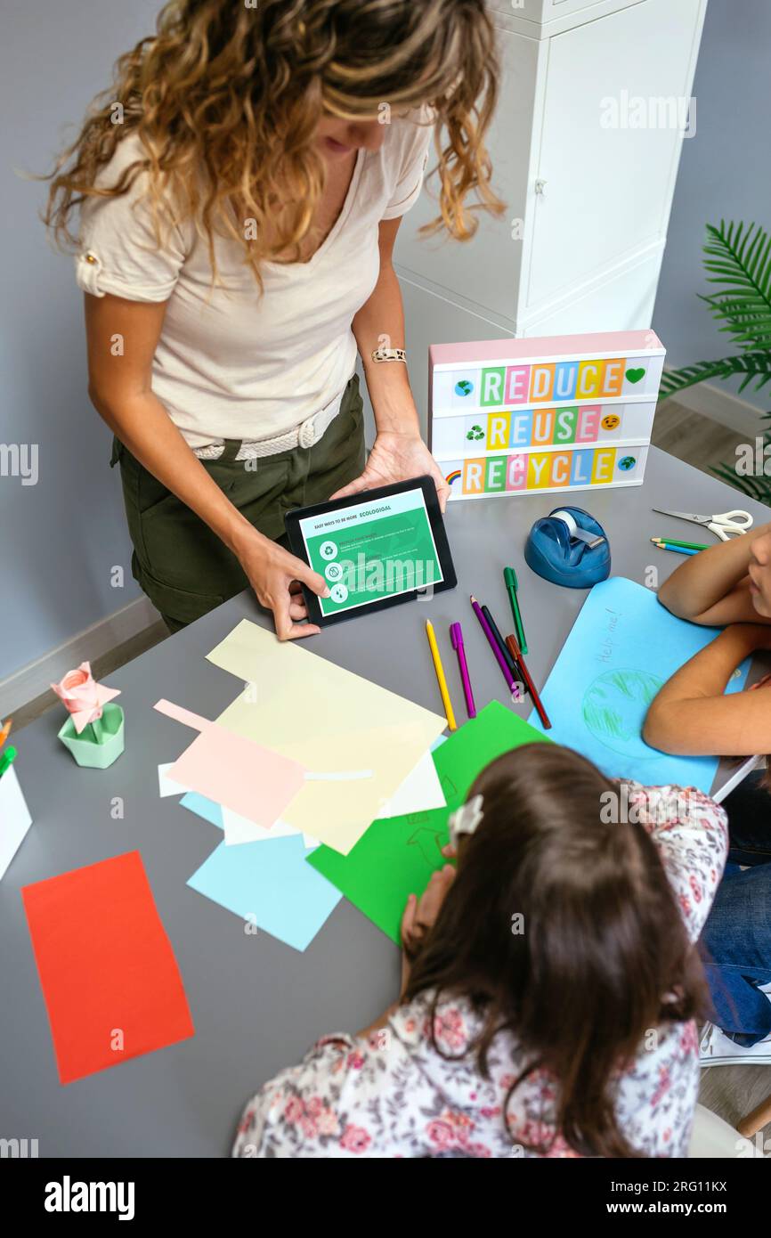 Unrecognizable female teacher showing electronic tablet with tips to be more ecological for young students in environmental classroom. Sustainable lif Stock Photo