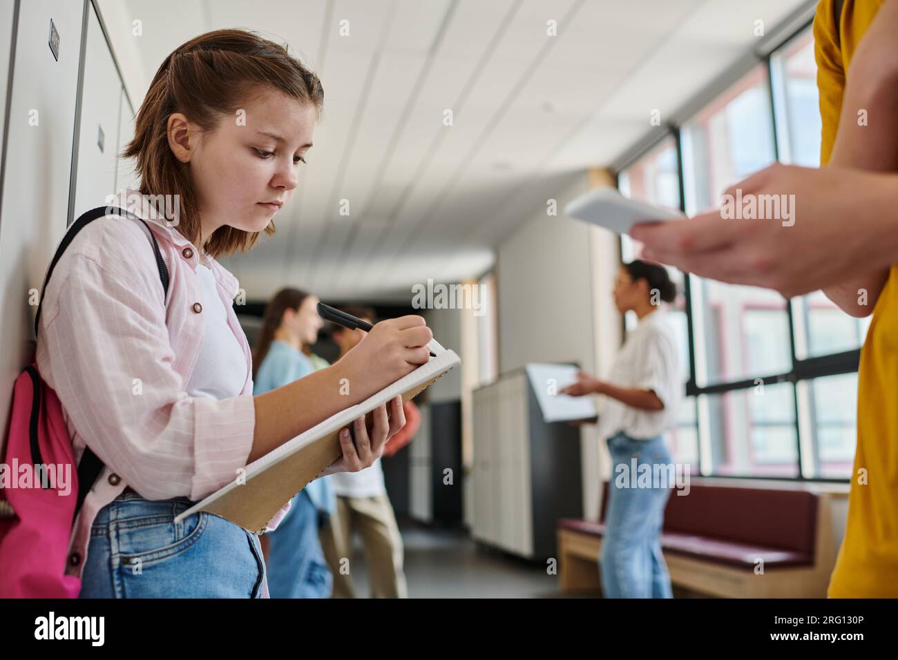 focused schoolgirl taking notes, holding notebook near boy using ...