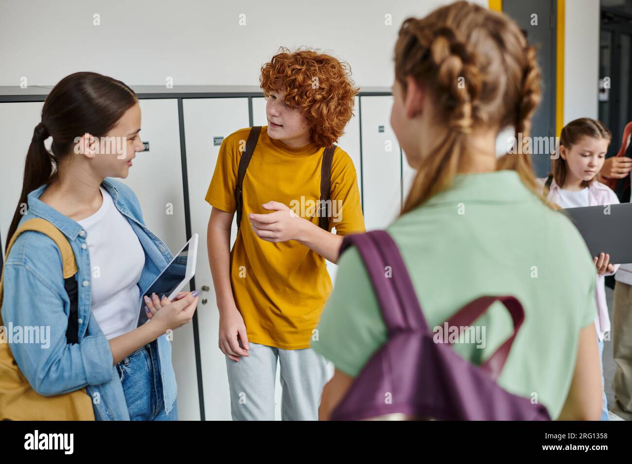 teenage classmates chatting in school hallway, teen students holding devices, youth culture, study Stock Photo