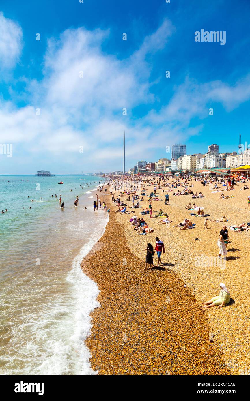 People sitting on the beach on a hot summer day with the burned down West Pier in background and the Brighton i360, Brighton, UK Stock Photo