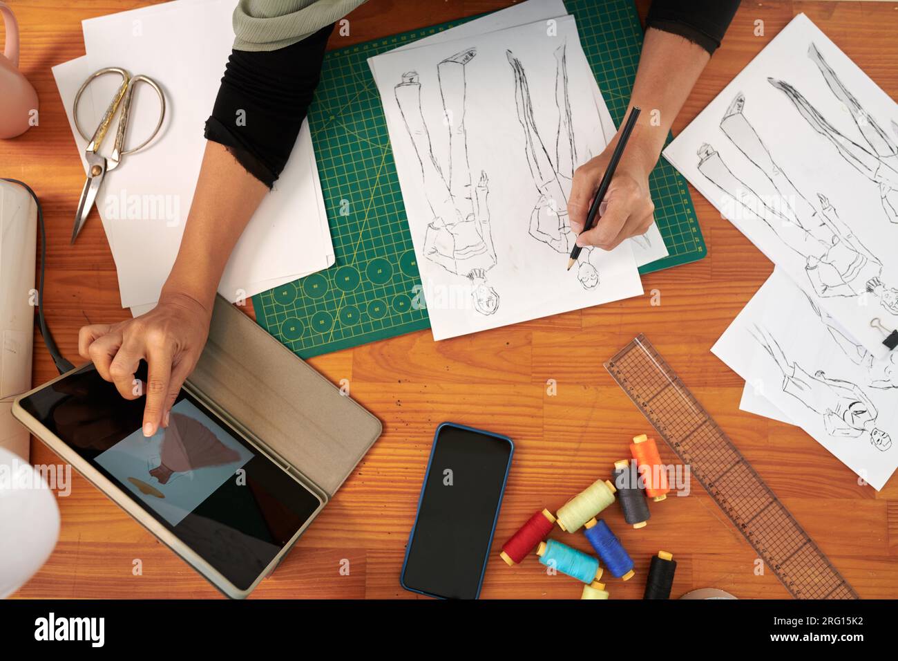 Hands of tailor drawing fashion sketch at her dek, view from above ...