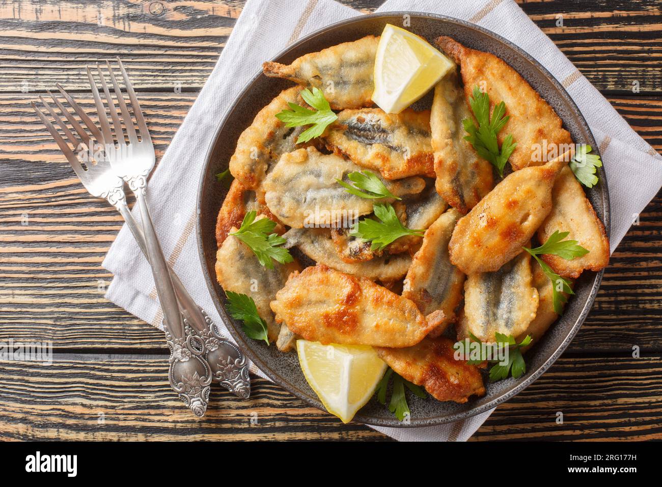 Plate of deep fried anchovies with lemon closeup on the table. Horizontal top view from above Stock Photo