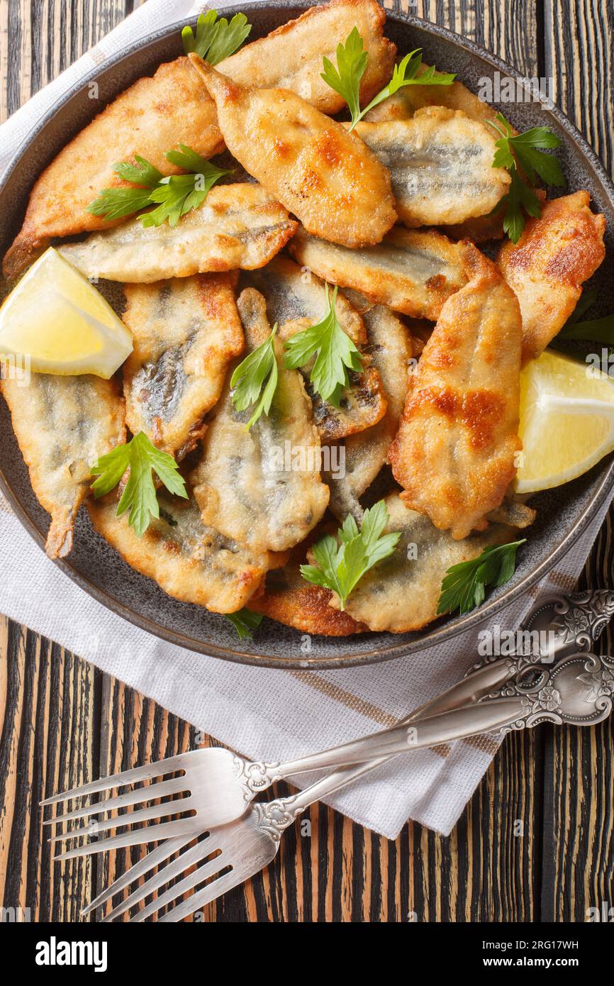 Delicious fried fillet anchovies sardines deep fried food served with lemon closeup on the table. Vertical top view from above Stock Photo