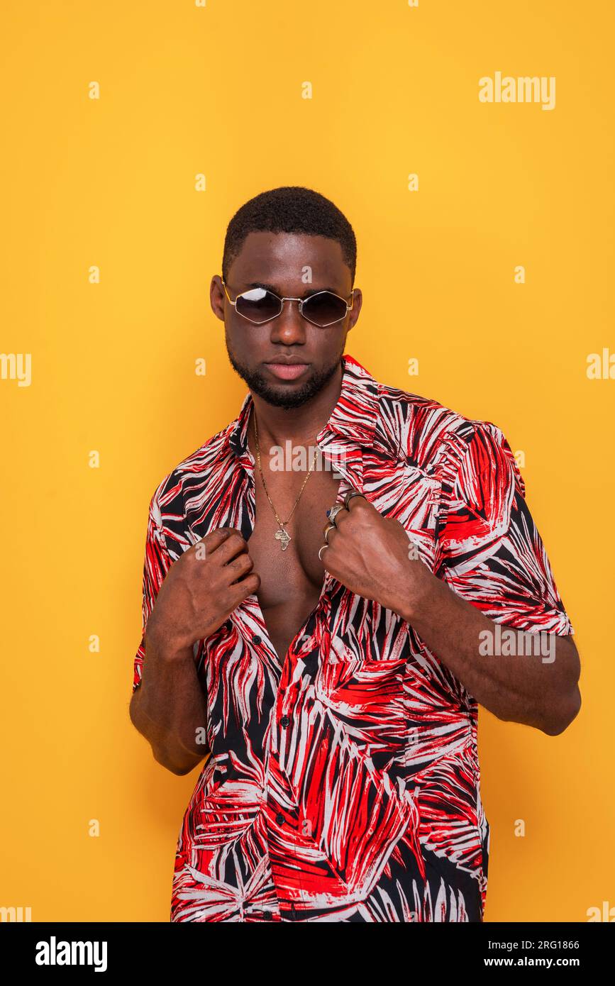 Portrait of serious young black male sunglasses in colorful unbuttoned  shirt with hands holding while standing on yellow background in studio  Stock Photo - Alamy