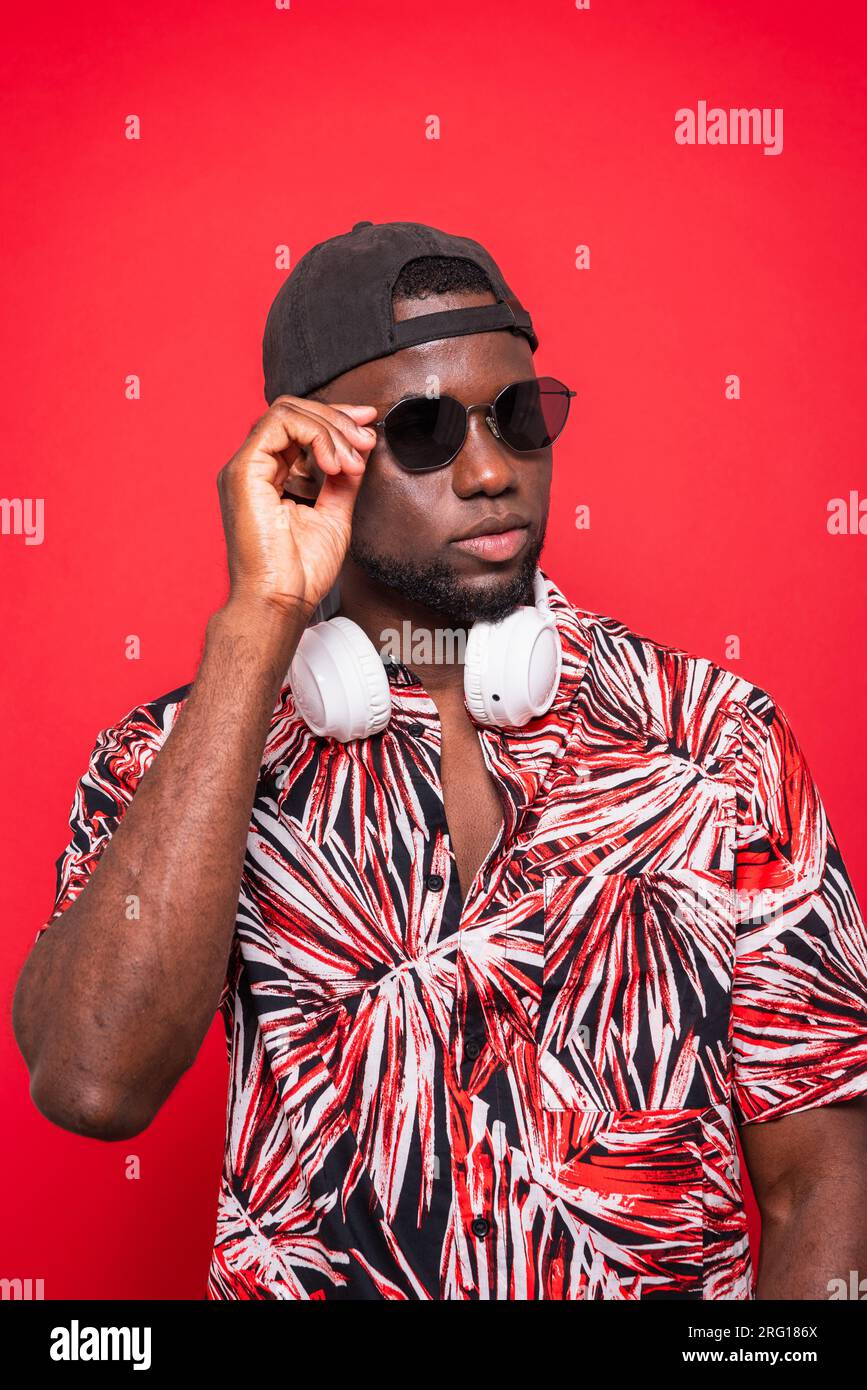 Portrait of man in sunglasses with cap worn backward and headphone by neck while in over red background Stock Photo