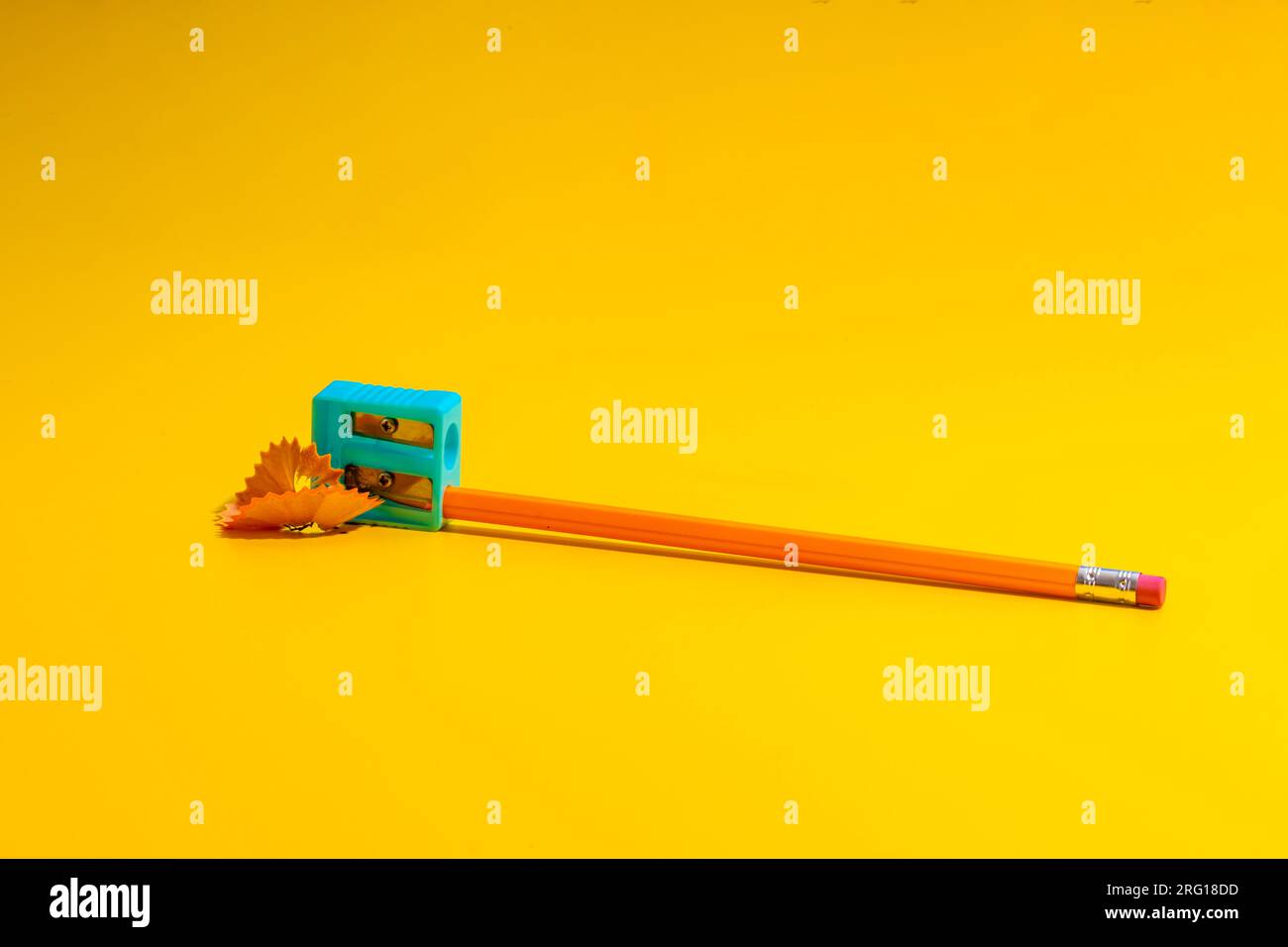 Simple pencil with eraser in plastic sharpener placed on yellow table near shavings Stock Photo