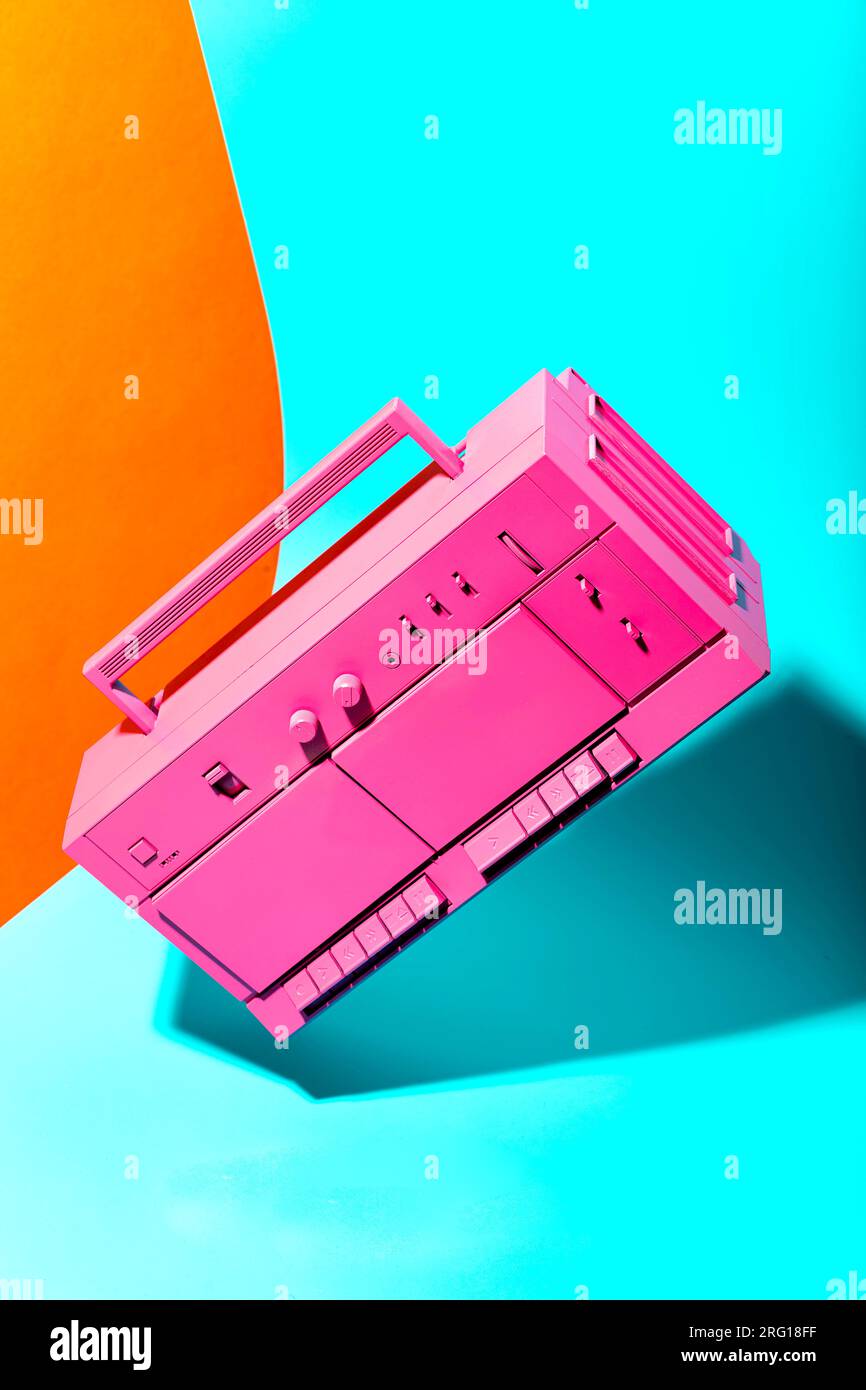 Pink colored retro boombox sound system placed on bright blue and yellow colors background Stock Photo