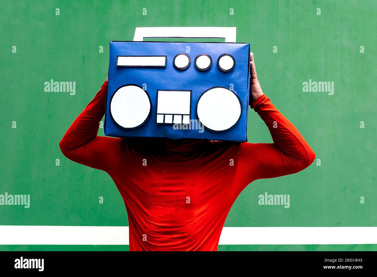 Unrecognizable person in red casual clothes standing with blue boombox covering face against green background Stock Photo