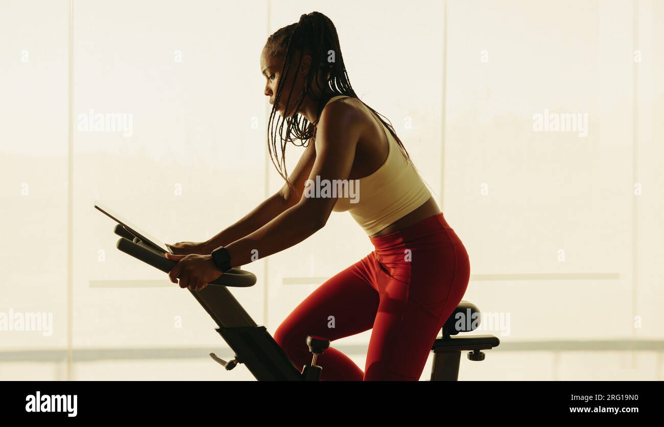 African American woman using an exercise bike to improve her cardio health and overall wellbeing. Young black woman engaging in fitness training in a Stock Photo