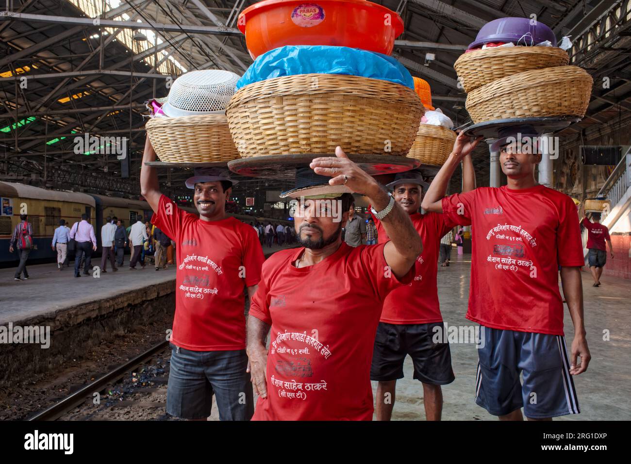Porters at Chhatrapati Shivaji Maharaj Terminus in Mumbai, India, laden with baskets on their heads, waiting for a local train to forward their goods Stock Photo