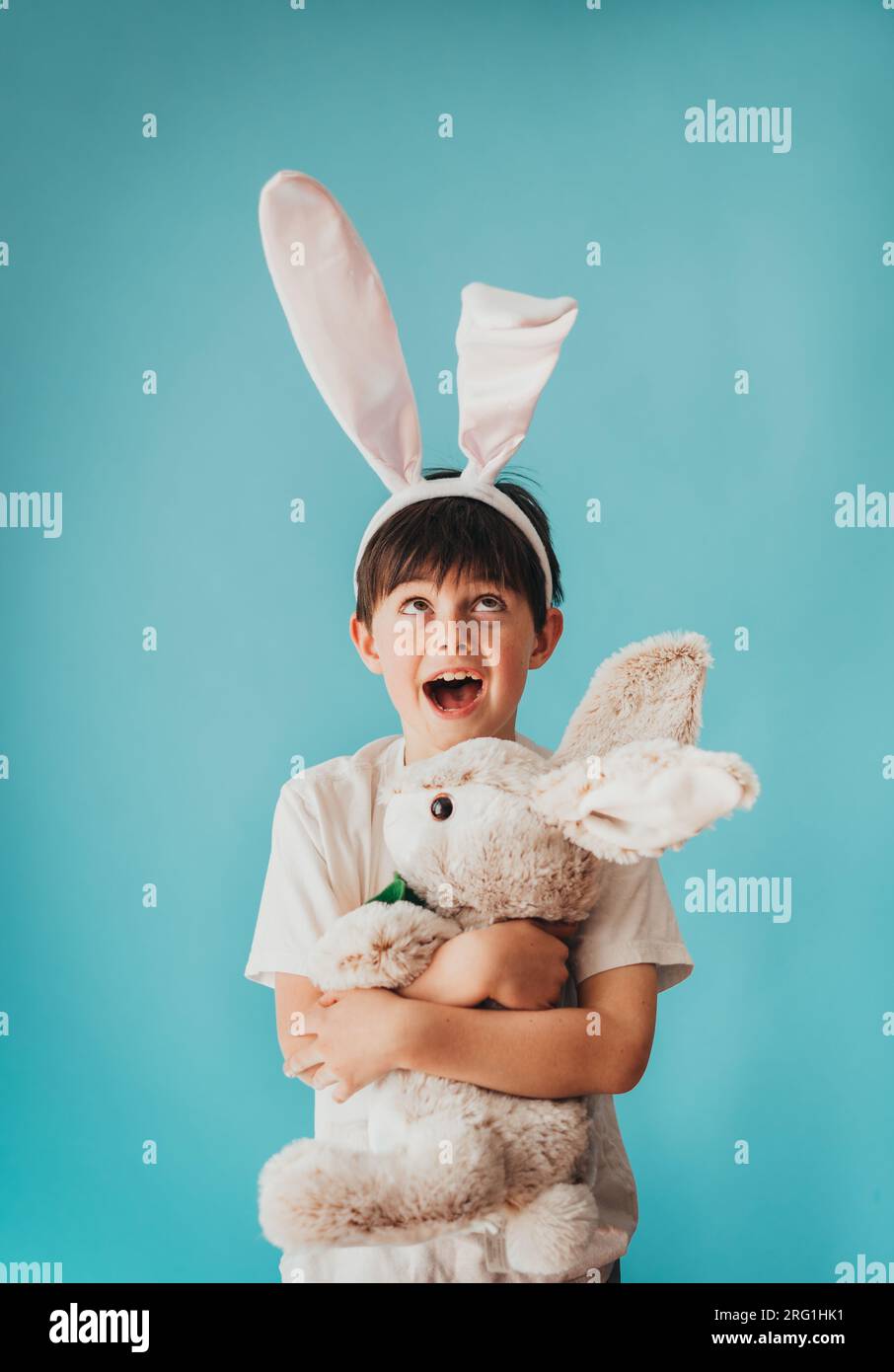 Boy holding stuffed rabbit looking up at bunny ears on his head. Stock Photo