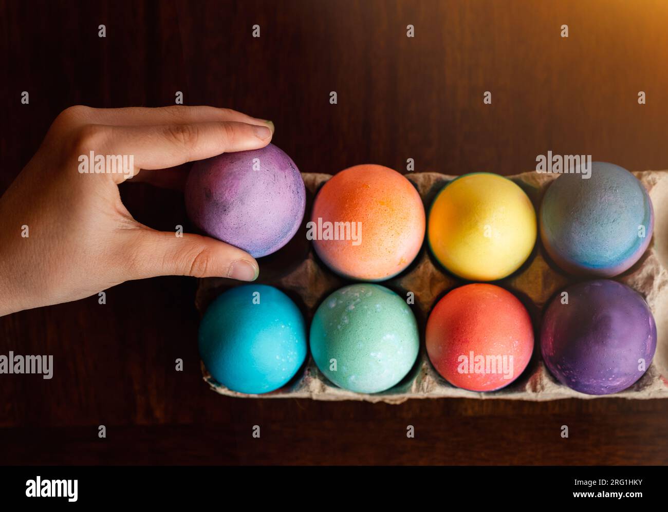 High angle of hand placing dyed egg with other colored Easter eggs. Stock Photo