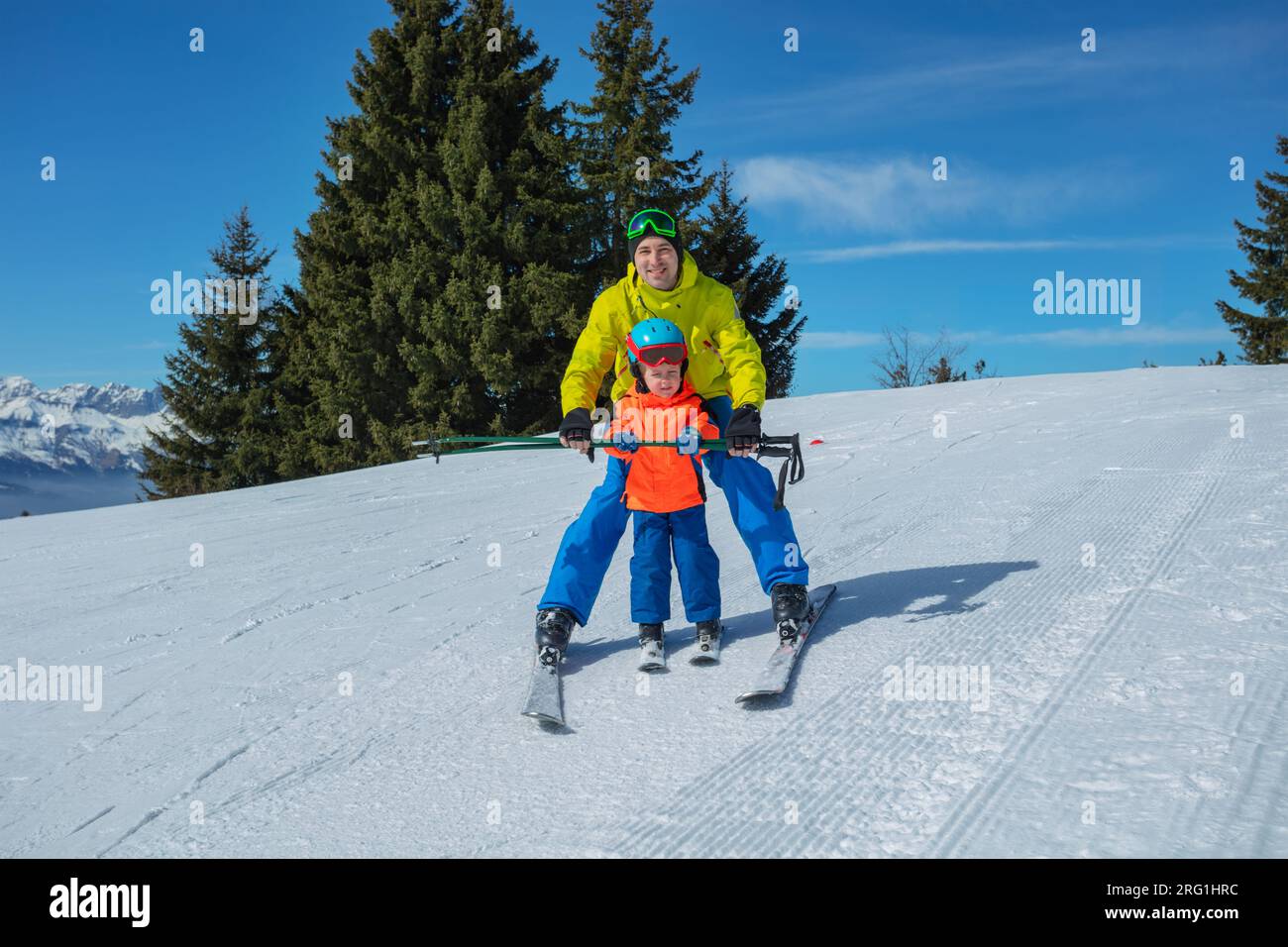 Instructor teaches kid gliding behind holding ski poles together Stock Photo