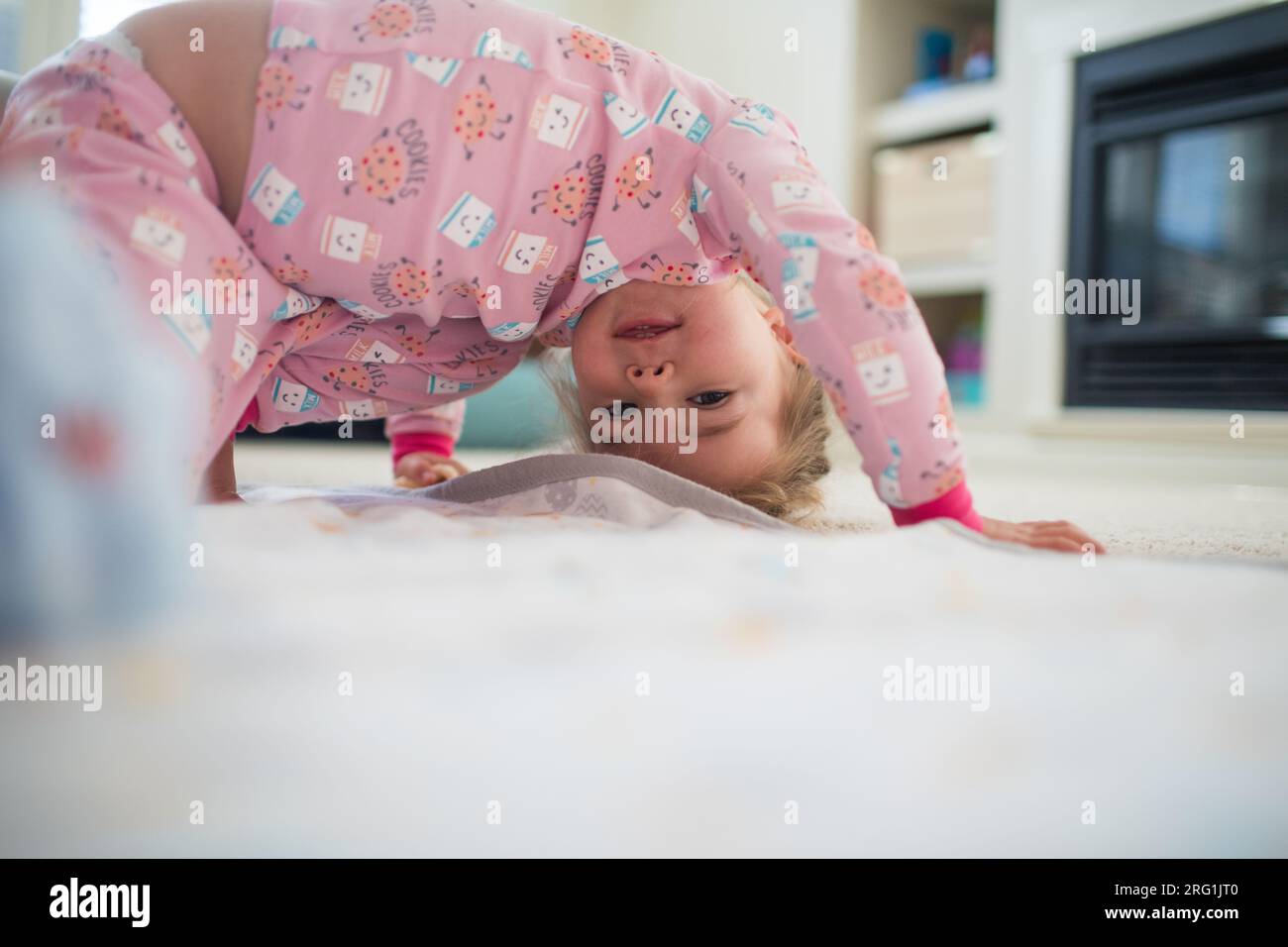 Young girl bend upside down, playing in living room at home. Stock Photo