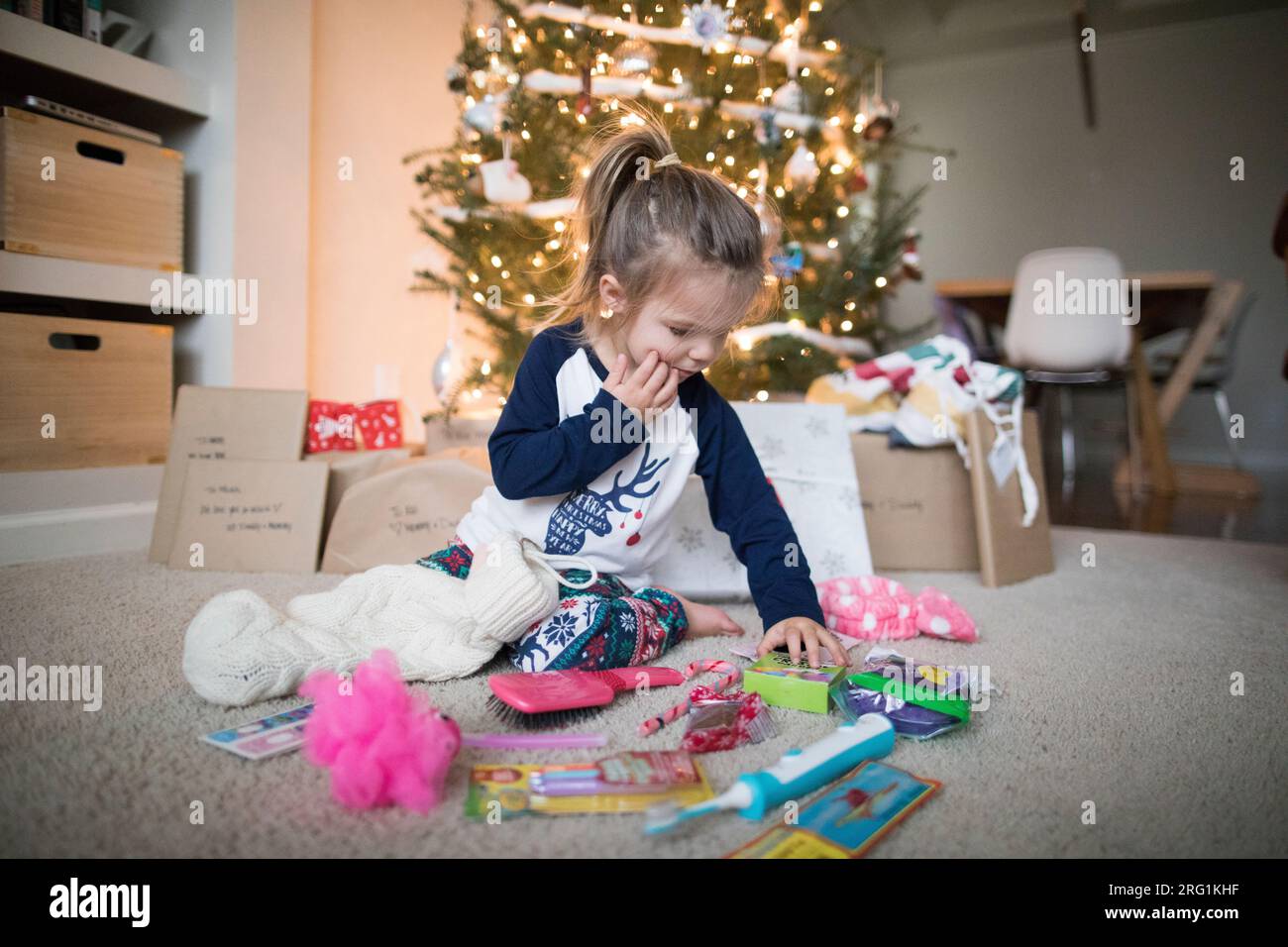 young girl spreads her gifts out under the Christmas Tree Stock Photo