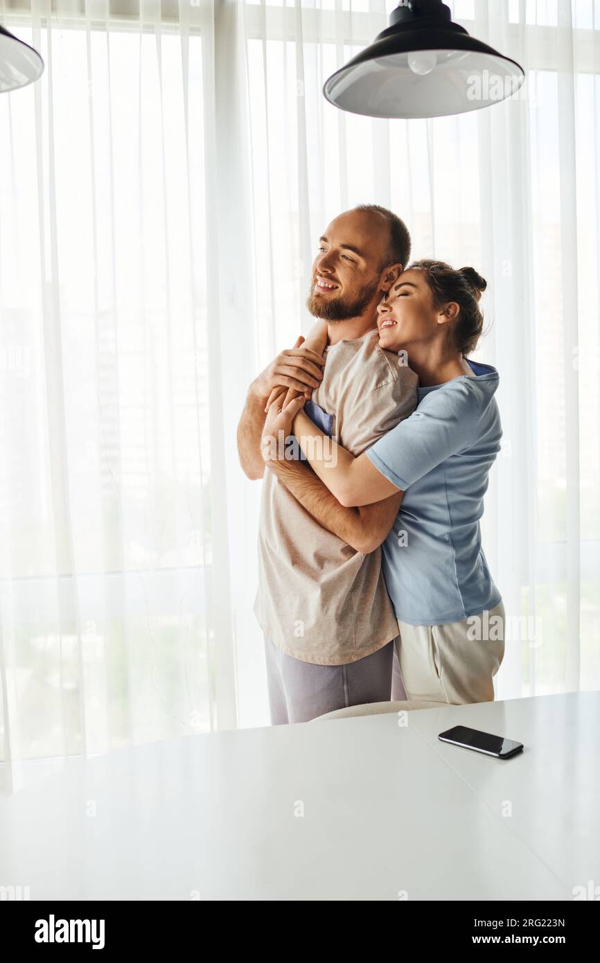 Smiling woman in homewear hugging boyfriend and standing near smartphone with blank screen at home Stock Photo