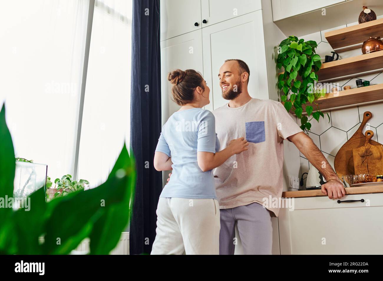 Smiling bearded man in homewear talking to girlfriend and standing together in kitchen at home Stock Photo