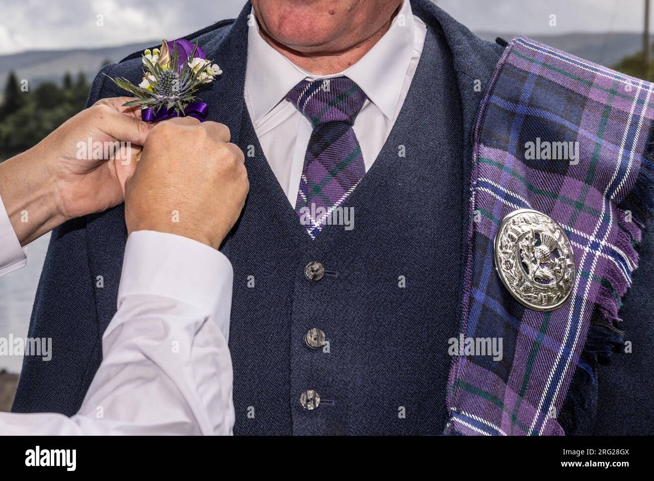 Groom in traditional Scottish dress getting ready for wedding getting help with button hole Stock Photo