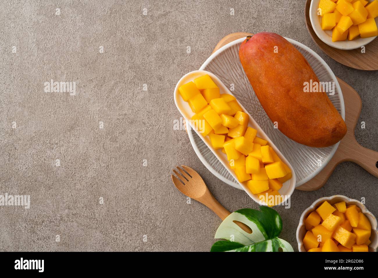 Fresh chopped, diced mango cubes on gray table background with tropical leaf for eating. Stock Photo