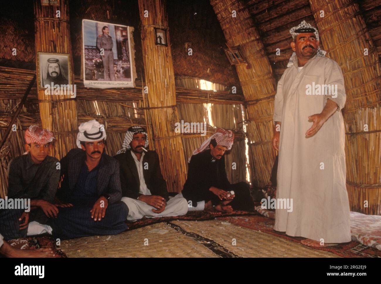 Marsh Arabs Iraq. Marsh Arab men in traditional reed building called Mudhif. There is a village meeting taking place. Photograph of Saddam Hussein on wall. Rivers Tigris and Euphrates wetlands, Hammar marshes. Southern Iraq 1980s 1984 HOMER SYKES Stock Photo