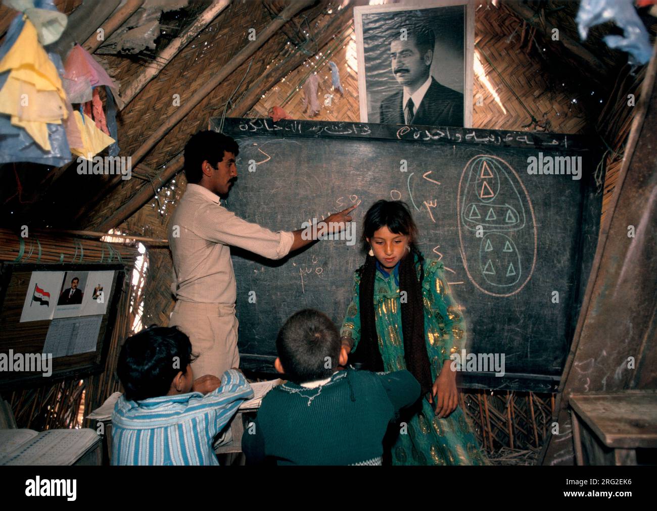 Marsh Arabs Southern Iraq.  Marsh Arab children in school a traditional reed constructed building. Portrait of Saddam Hussein hanging from wall. Rivers Tigris and Euphrates wetlands, Hammar marshes. Southern Iraq 1980s 1984 HOMER SYKES Stock Photo