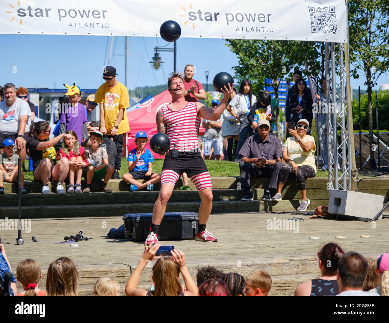 Strongman busker Mighty Mike juggling three bowling balls to crowd