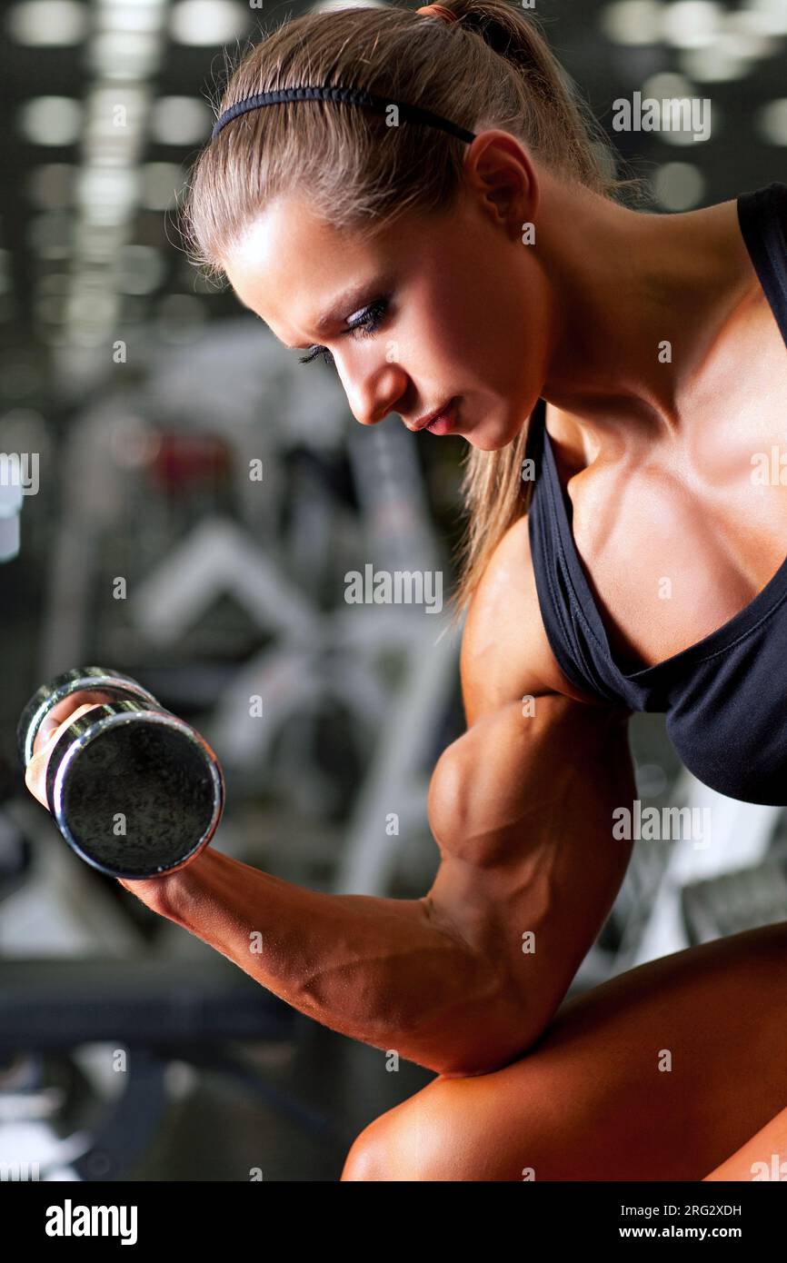 Beautiful girls with long hair is training in the gym with weights. Personal  fitness trainer is at work doing exercises for good muscles. Sport  motivation healthy lifestyle. Woman body workout. Stock Photo