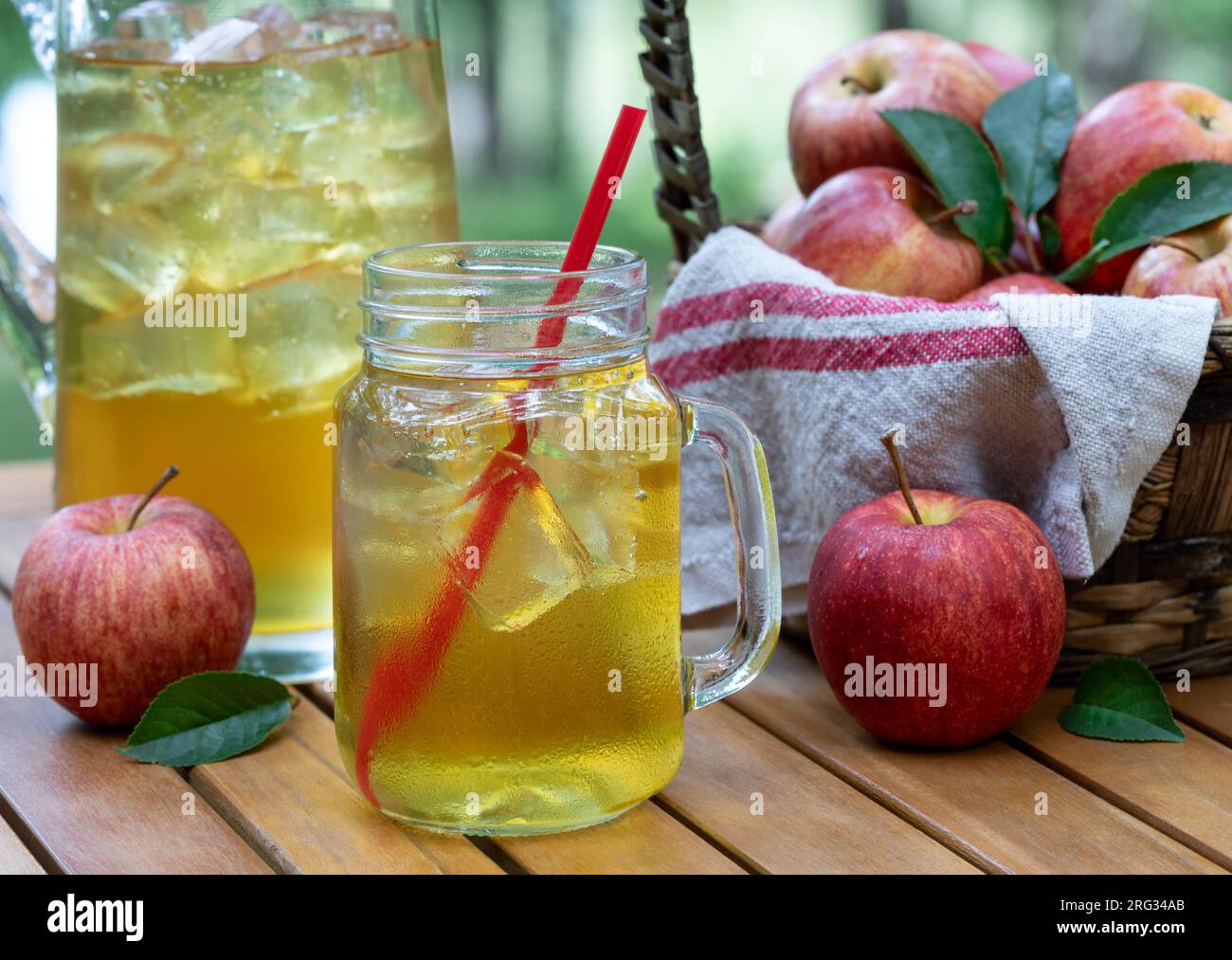 Apple juice in glass jar and pitcher with fressh red apples outdoors on wooden patio table and nature background Stock Photo