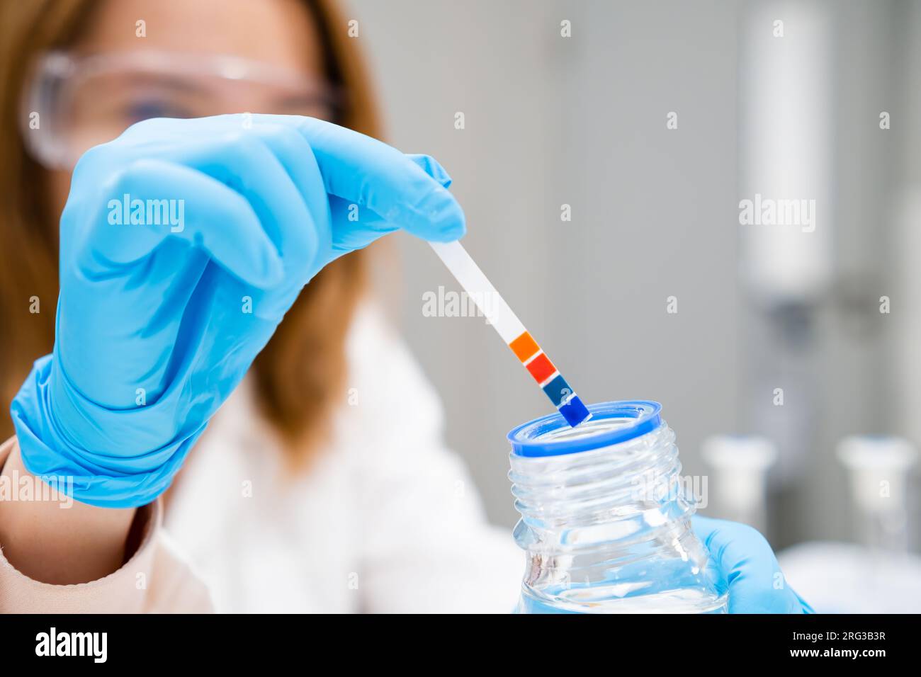 Young female scientist in white lab coat measures pH of the solution using indicator paper.  Stock Photo