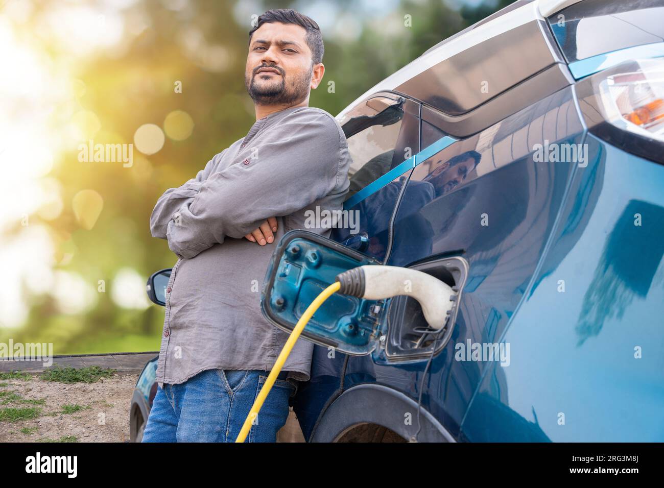 Indian man standing while his modern electric car getting charge at