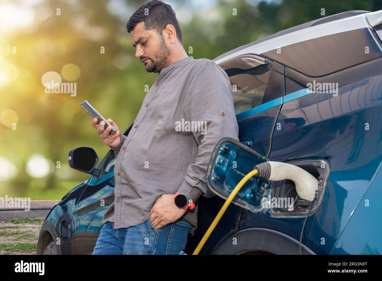 Indian man using smartphone while his modern electric car getting
