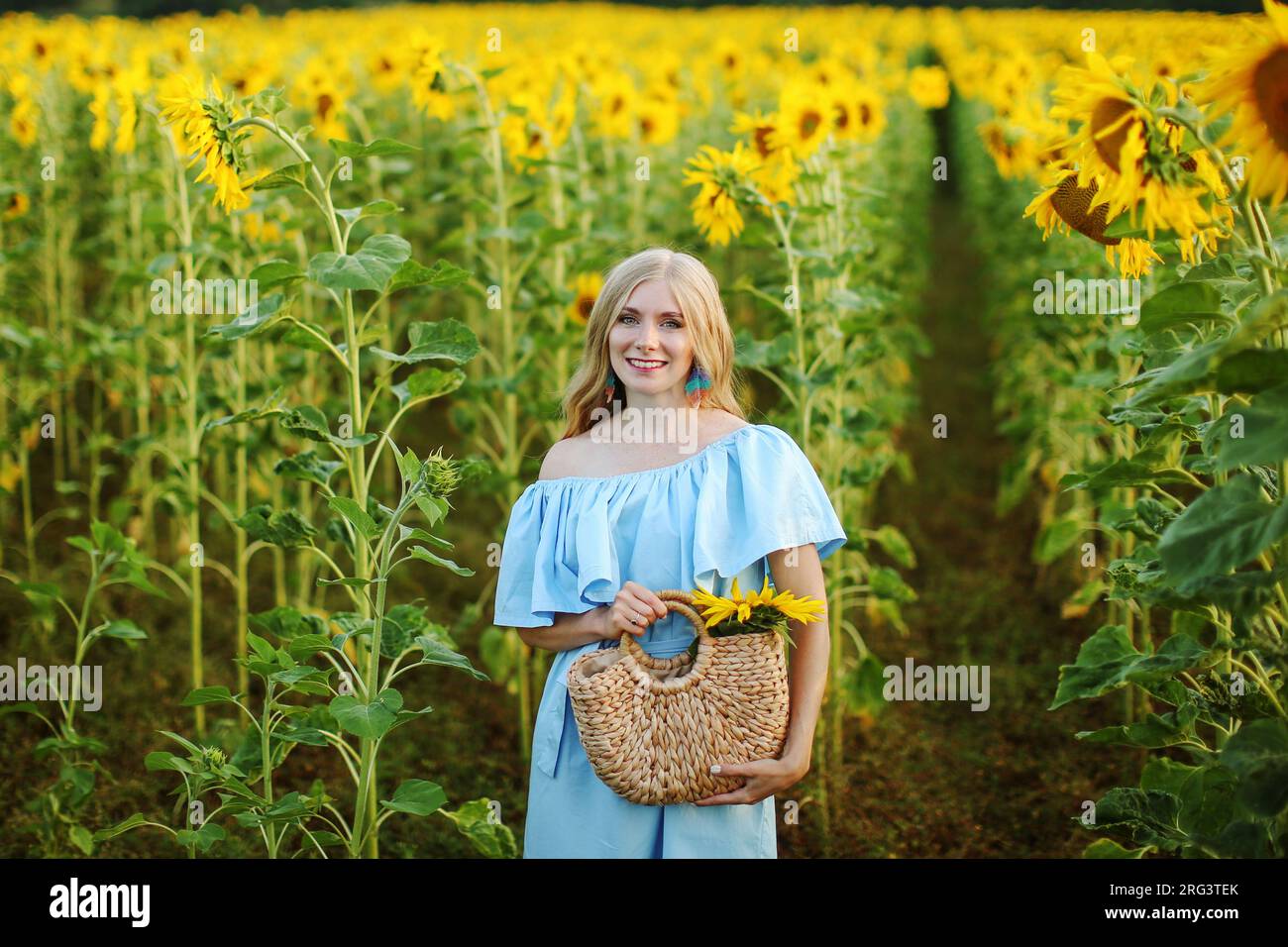 portrait of a young woman with long and fair hair standing in a field ...