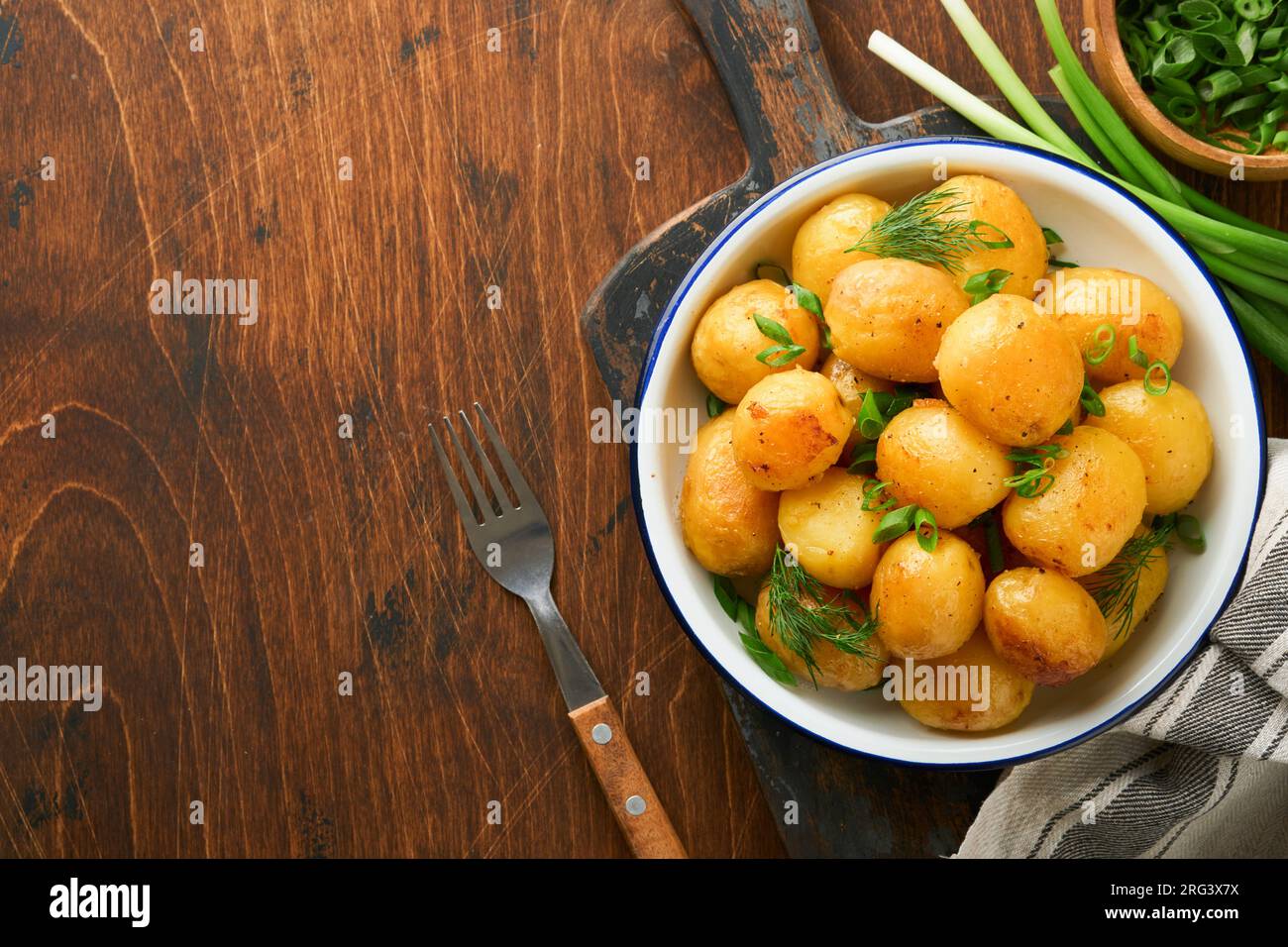 Boiled new or young potatoes with butter, fresh dill and onions in white bowl on dark old rustic wooden background. Tasty new boiled potatoes. Top vie Stock Photo