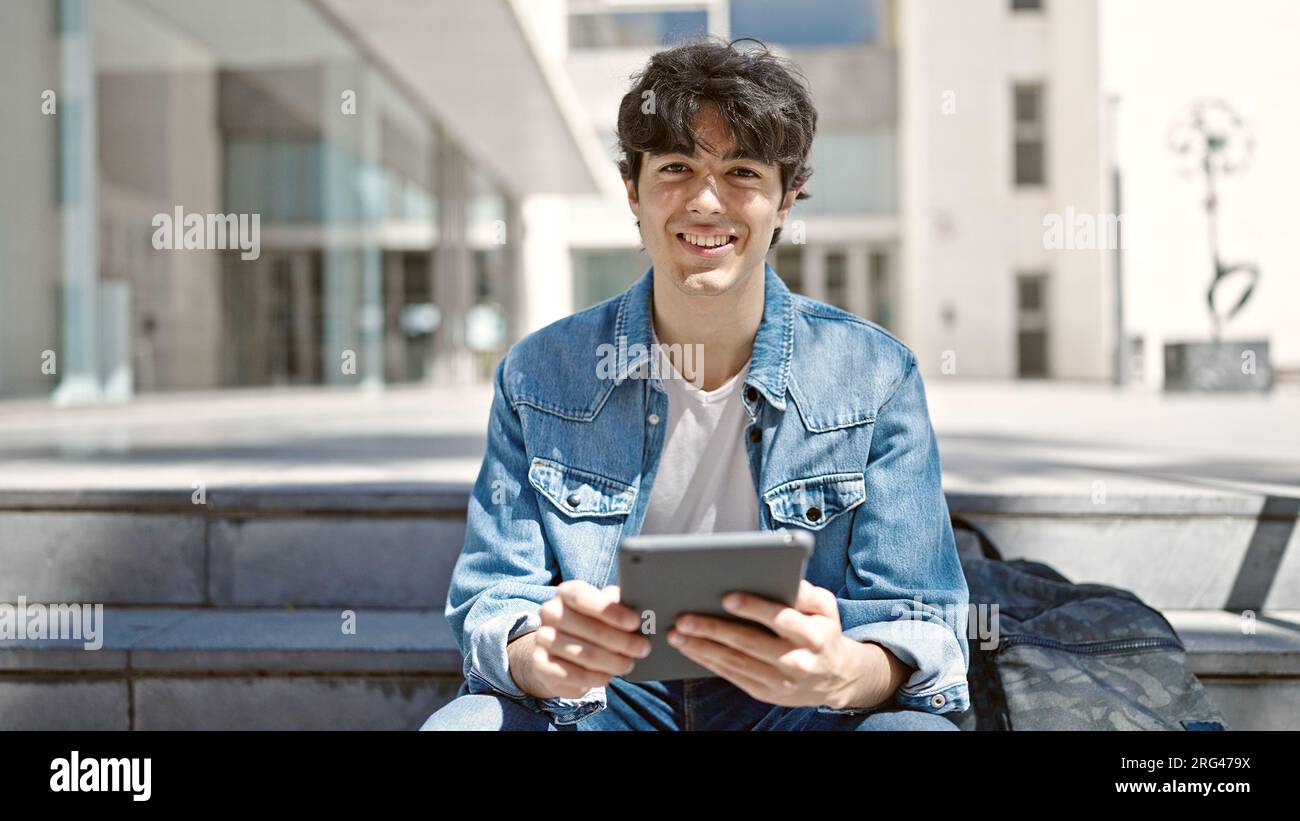 Young hispanic man student using touchpad sitting on stairs at ...
