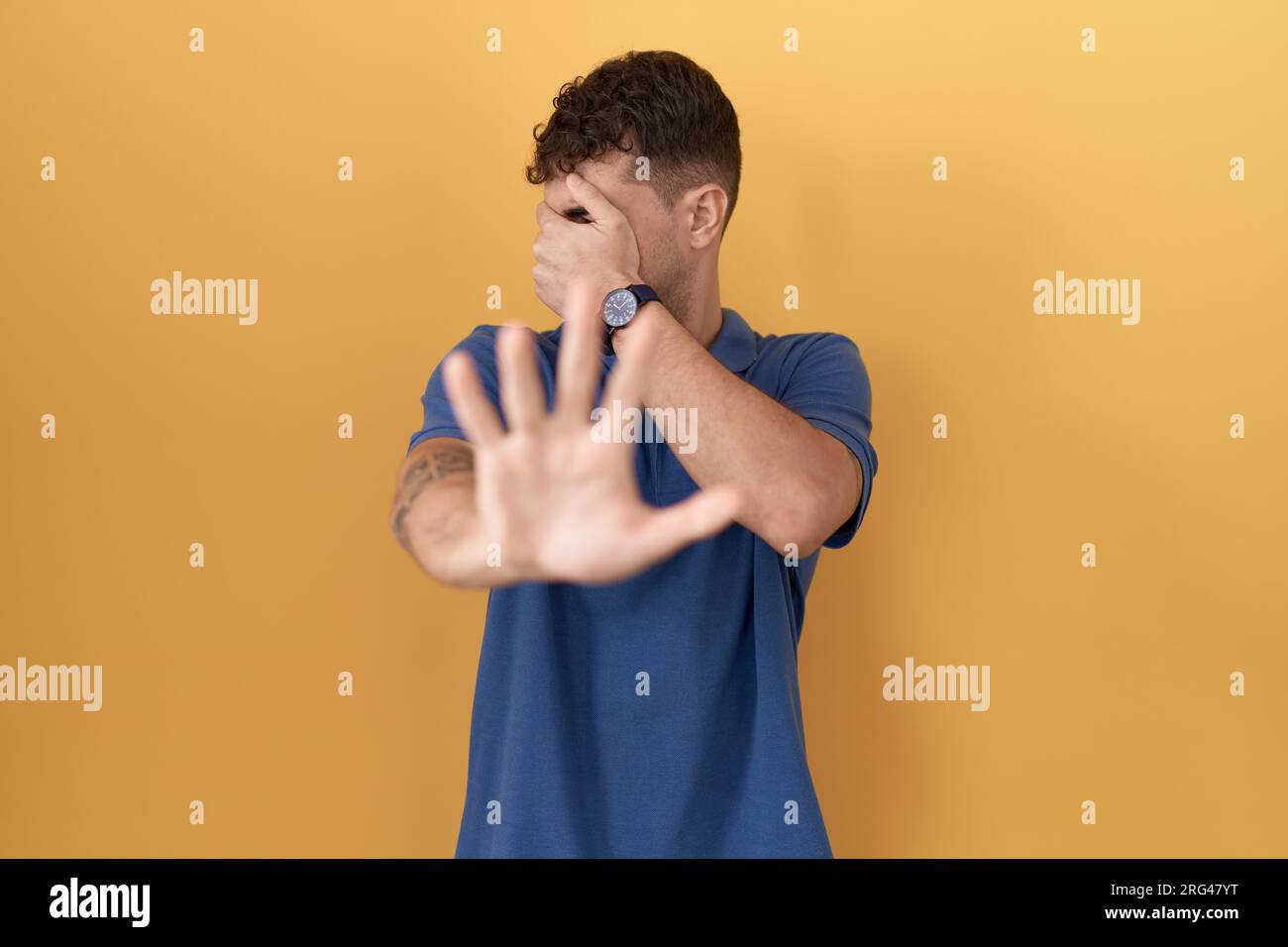 Young hispanic man standing over yellow background covering eyes with hands and doing stop gesture with sad and fear expression. embarrassed and negat Stock Photo