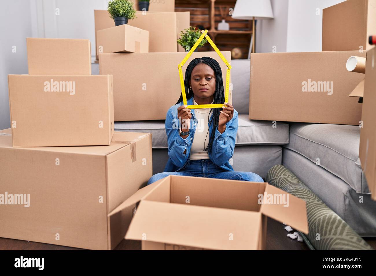 African woman with braids sitting on the floor at new home holding ...