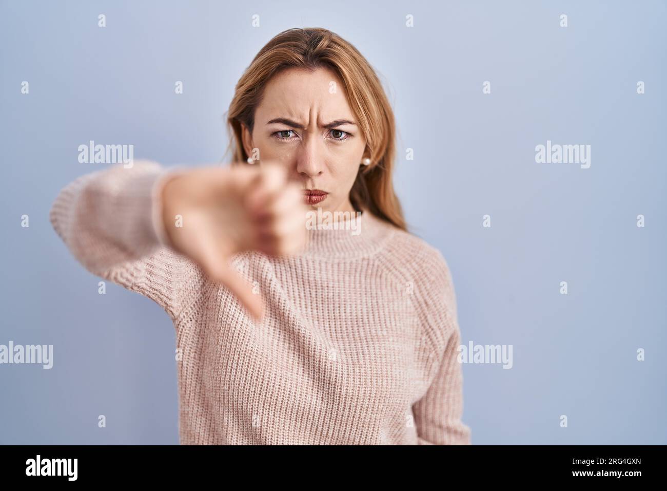 Hispanic woman standing over blue background looking unhappy and angry ...