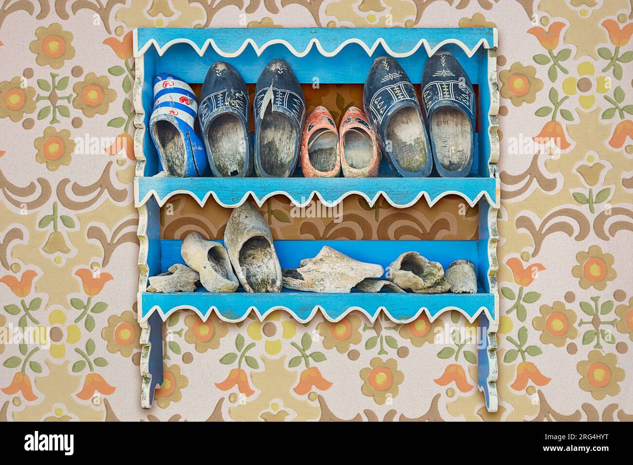 Old cabinet with weathered vintage Dutch wooden clogs on a wall with retro wallpaper Stock Photo